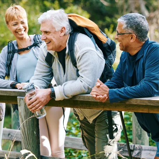 A group of seniors go for a hike and stop to talk on a bridge