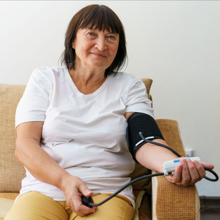 Senior woman checking blood pressure on couch