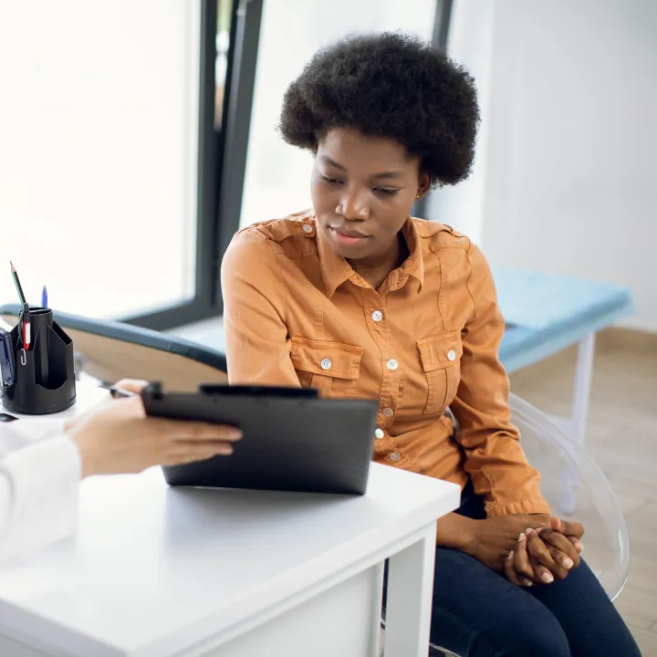 Doctor reviews clipboard with Black patient looking down in a clinic.