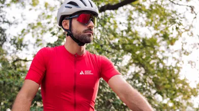 A man in a cycling helmet and red ADA Tour de Cure cycling shirt looking into the distance