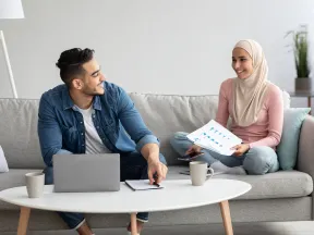 man and woman sitting on couch talking with laptop