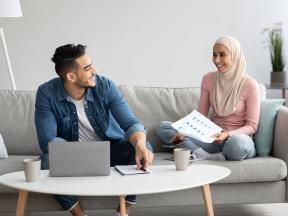 man and woman sitting on couch talking with laptop