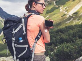 A woman monitors her blood sugar CGM while hiking.