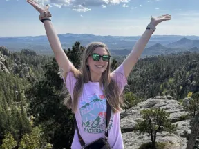 A woman on a mountain top with her arms raised.