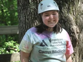 Smiling girl in a helmet, harness, and ADA Camp Midich t-shirt.