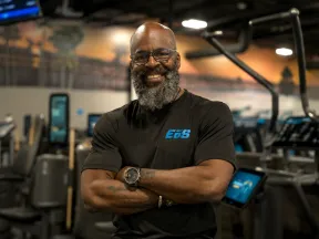 Confident man with beard smiles, arms crossed, in a modern gym.