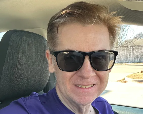 A man wearing sunglasses and a purple t-shirt.