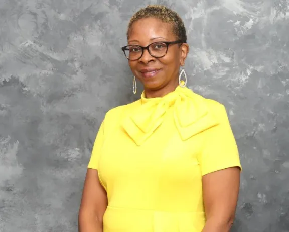 Photo of woman in yellow standing in front of gray background.