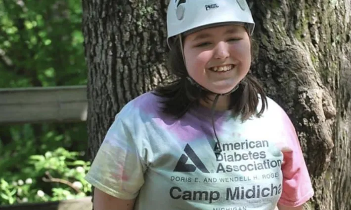 Smiling girl in a helmet, harness, and ADA Camp Midich t-shirt.