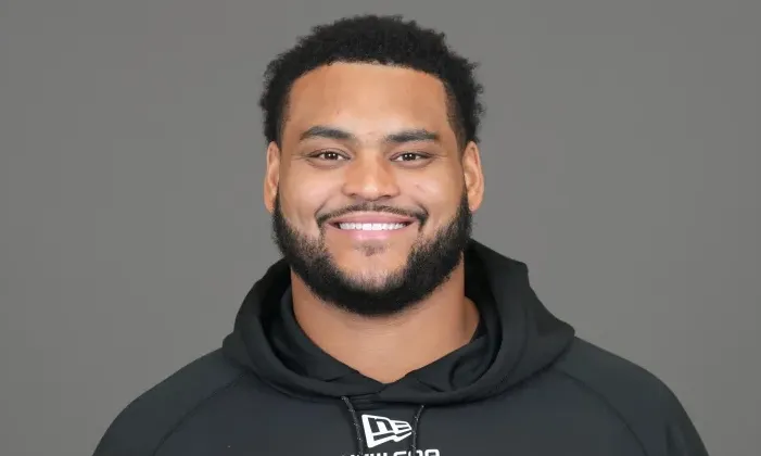 Smiling man with a beard and dark hair, wearing a black hoodie.