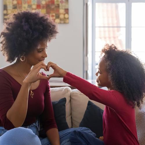 A mother and her daughter make heart shapes with their hands.
