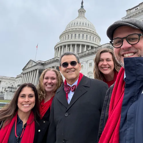 Five smiling people in red scarves pose in front of the U.S. Capitol Building.