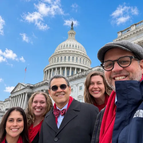 Five smiling people, some in red, with the U.S. Capitol Building in background.