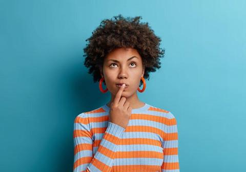 Young woman with finger pressed to her lips thinking about how to solve a problem