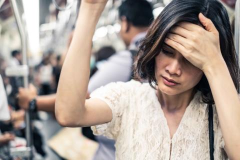 Asian woman on subway feeling ill with hand on forehead