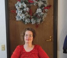 Photo of Christine sitting front of a door with a wreath.