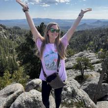 A woman on a mountain top with her arms raised.