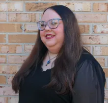 A woman standing in front of a brick wall.
