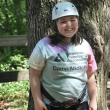 Smiling girl in a helmet, harness, and ADA Camp Midich t-shirt.