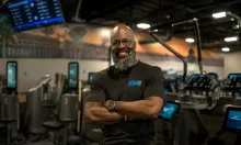 Confident man with beard smiles, arms crossed, in a modern gym.