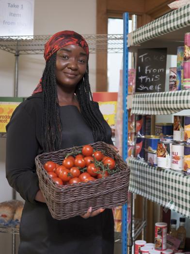 african american woman standing in food pantry holding a basket of tomatoes