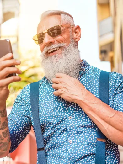 A senior man is wearing sunglasses and smiling at his phone